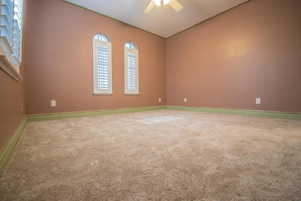 Bedroom with new beige wall-to-wall carpet, terracotta walls and two arched shuttered windows