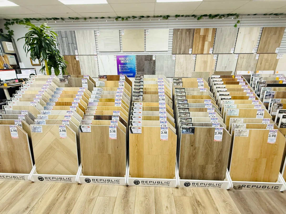Rows of floor-standing vinyl plank sample racks in the Vegas Flooring Outlet showroom, with a sample wall behind them