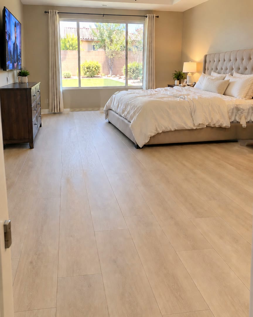 Una recámara con piso vinílico SPC claro con aspecto de madera, una cama tendida, mesitas de noche y una ventana grande